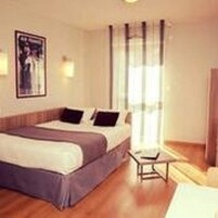 Una habitación de hotel con una cama, una mesita de noche, una ventana con cortinas y un aplique de pared.