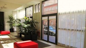 A hotel lobby with a red bench, potted plants, and a view of the street through large glass doors.