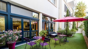 An outdoor patio with purple chairs and tables, a red umbrella, and a small grill. - Privilège Appart Hotel Saint-Exupéry (Toulouse)