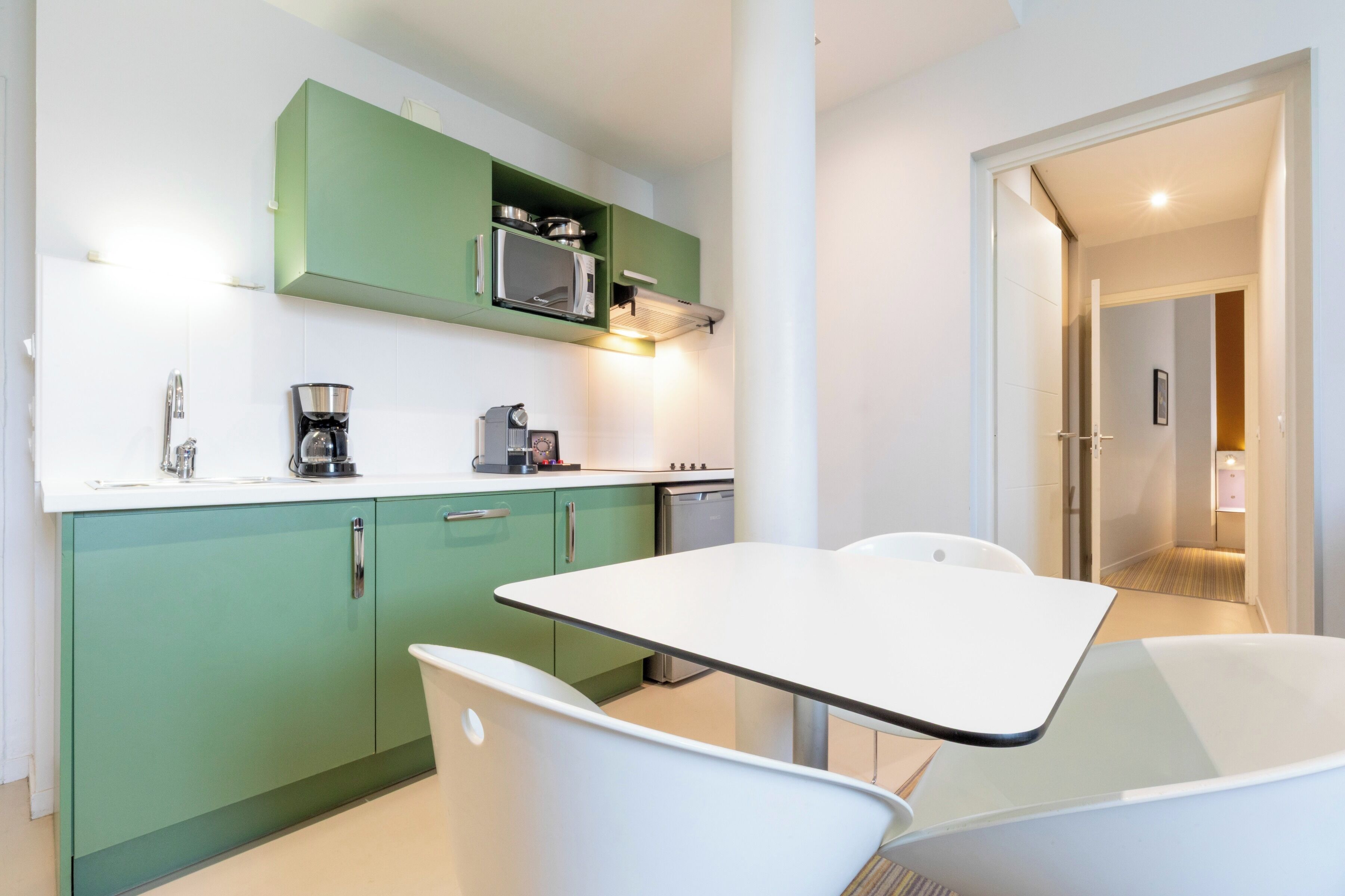 Una cocina compacta con armarios verdes, una encimera blanca y una mesa de comedor con sillas.