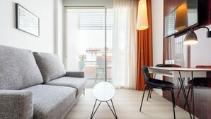 A modern living room with a grey sofa, a round white side table, a black chair, a wooden dining table, and a large window with curtains. - Privilège Appart Hotel Saint-Exupéry (Toulouse)
