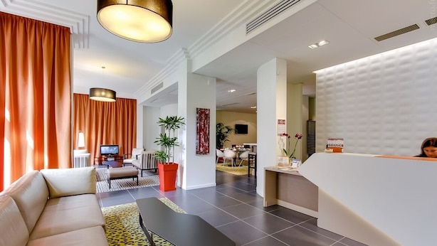 A modern hotel lobby with a reception desk, seating area, and a television. - Privilège Appart Hotel Saint-Exupéry (Toulouse)