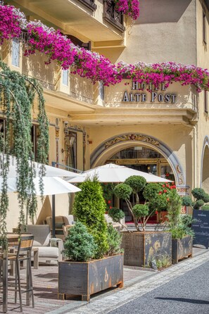A hotel entrance with a sign reading 'HOTEL ALTE POST,' outdoor seating with umbrellas, and potted plants. - Hotel Alte Post (Sankt Anton am Arlberg)