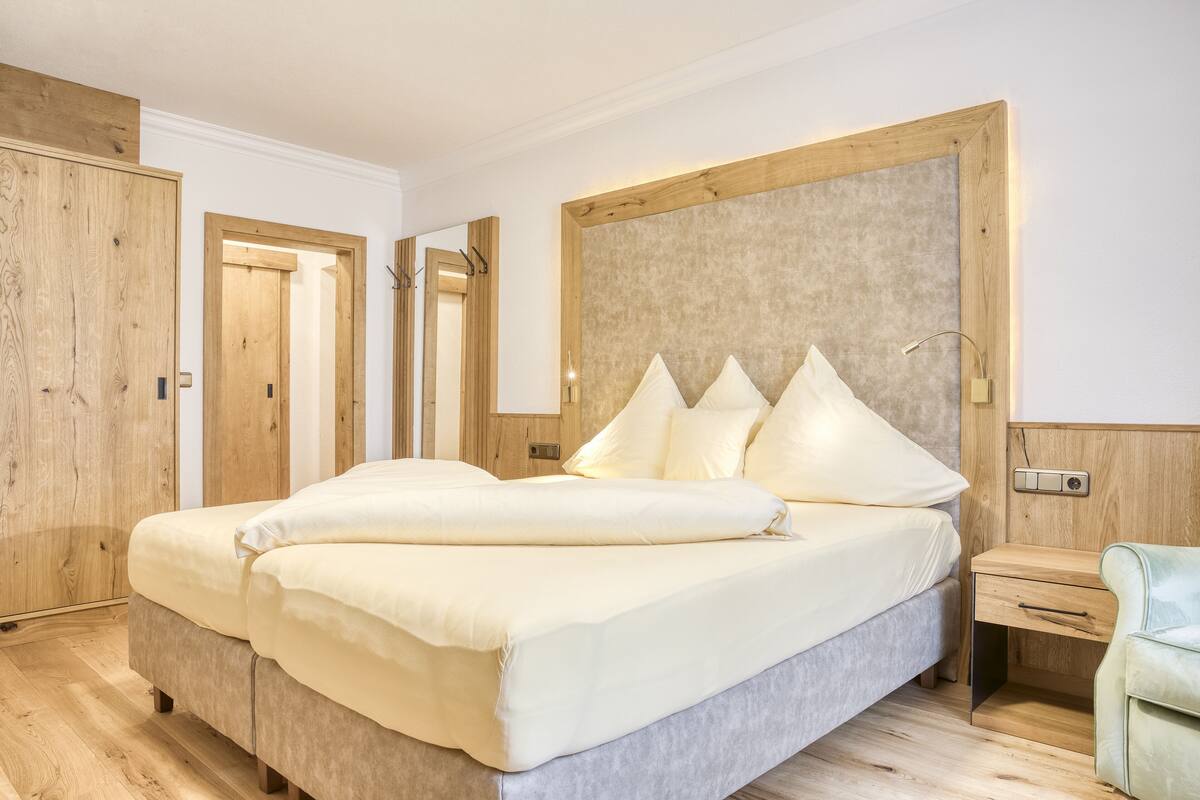 A bedroom with a large bed, wooden wardrobe, and a mirror.