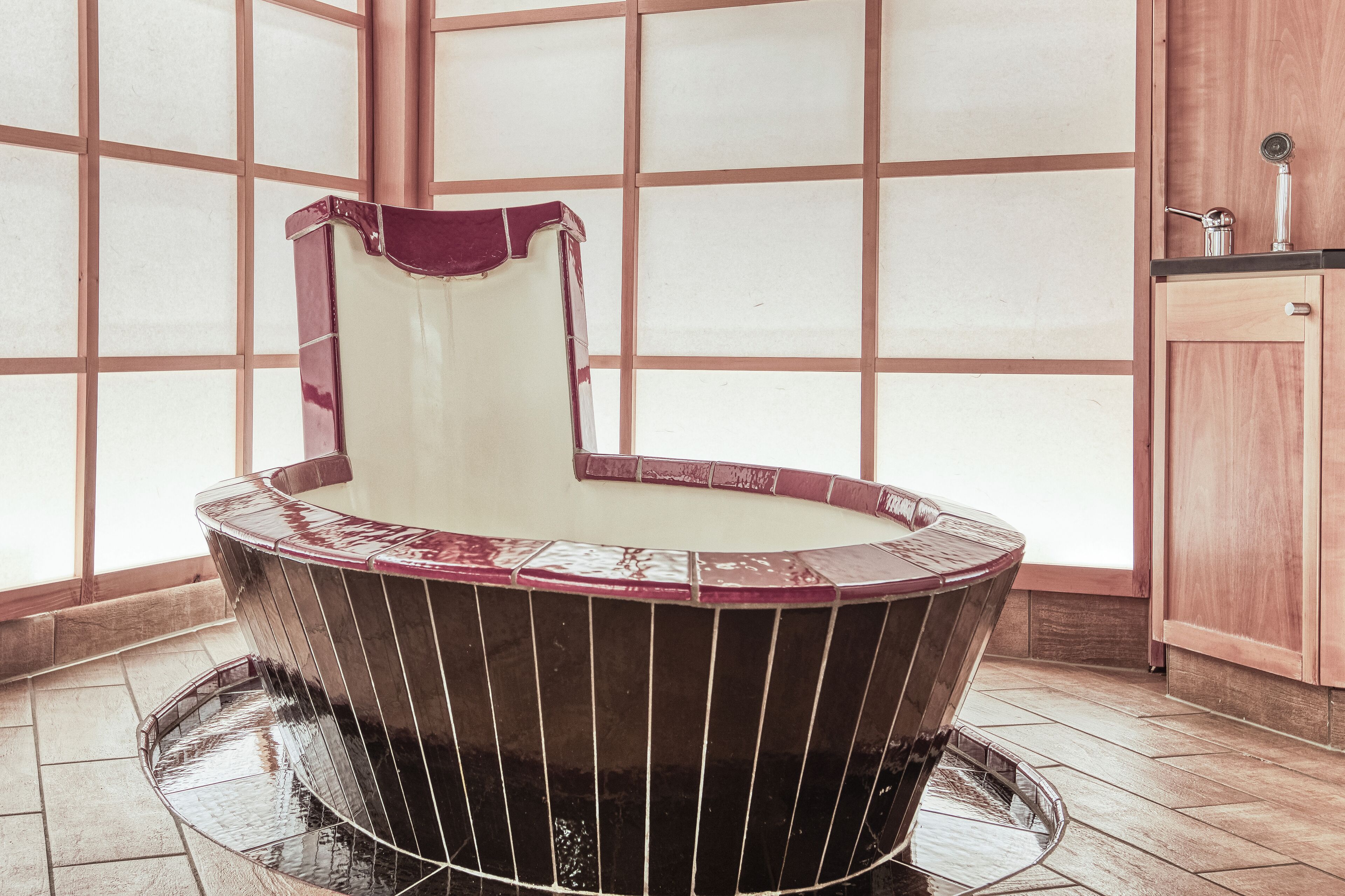 Una vasca da bagno ad angolo dal design curvo, un mobile in legno sulla destra e un pavimento piastrellato.