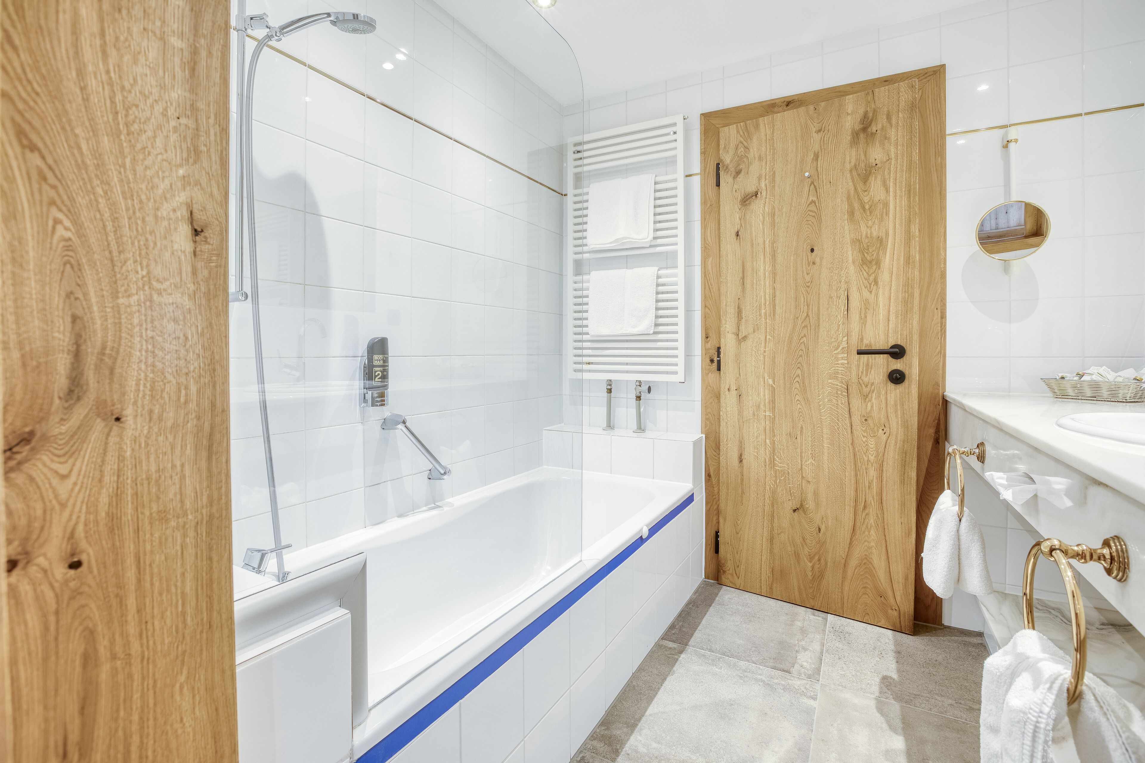 Un baño moderno con cabina de ducha de vidrio, una puerta de madera y piso de baldosas blancas.