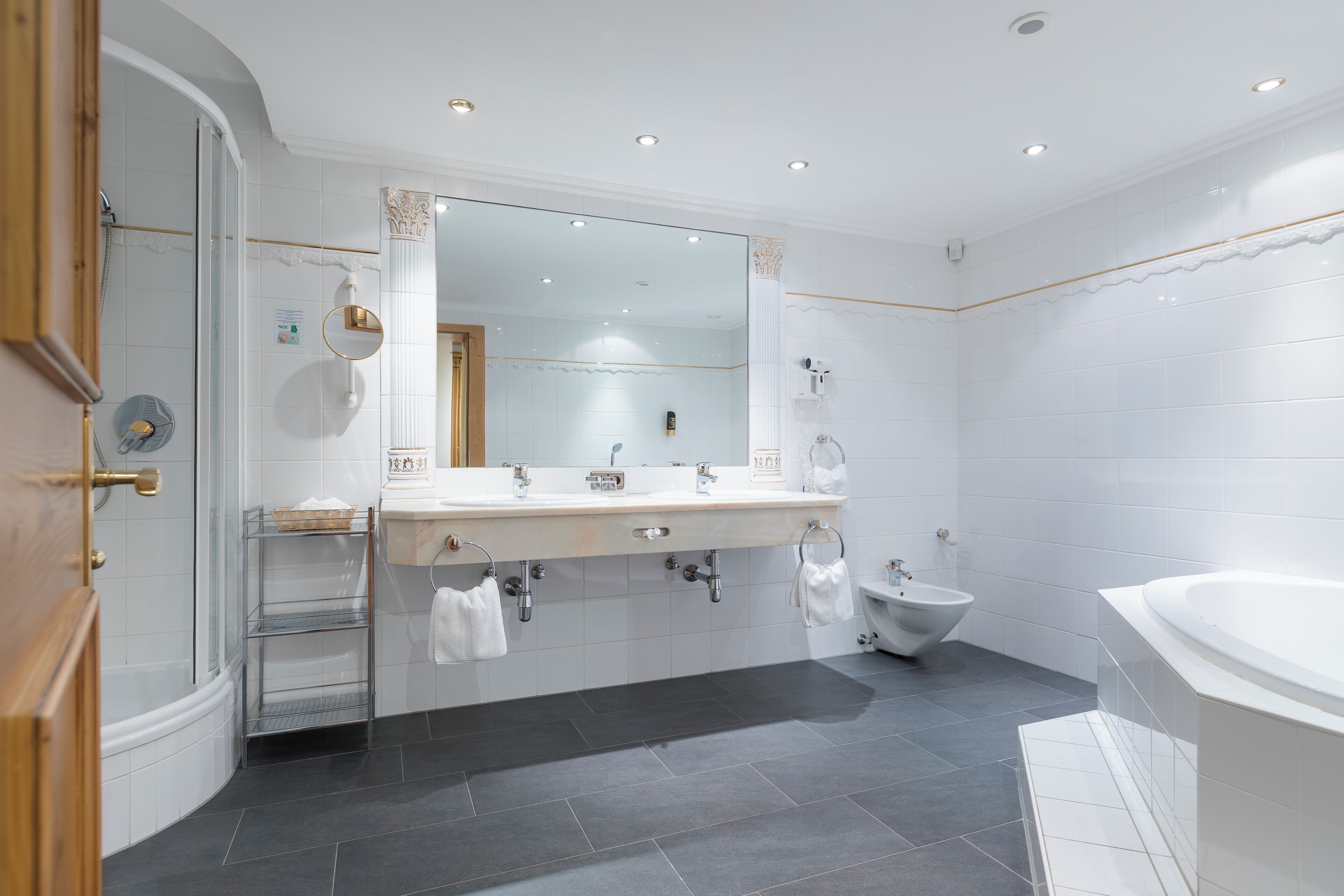 Une salle de bain moderne avec un grand miroir, deux lavabos, un bidet et une baignoire.