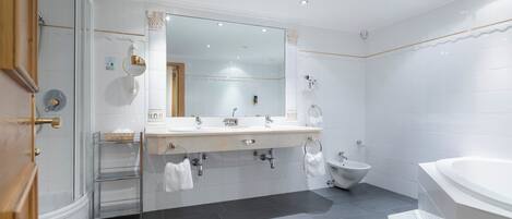 A modern bathroom with a large mirror, two sinks, a bidet, and a bathtub.