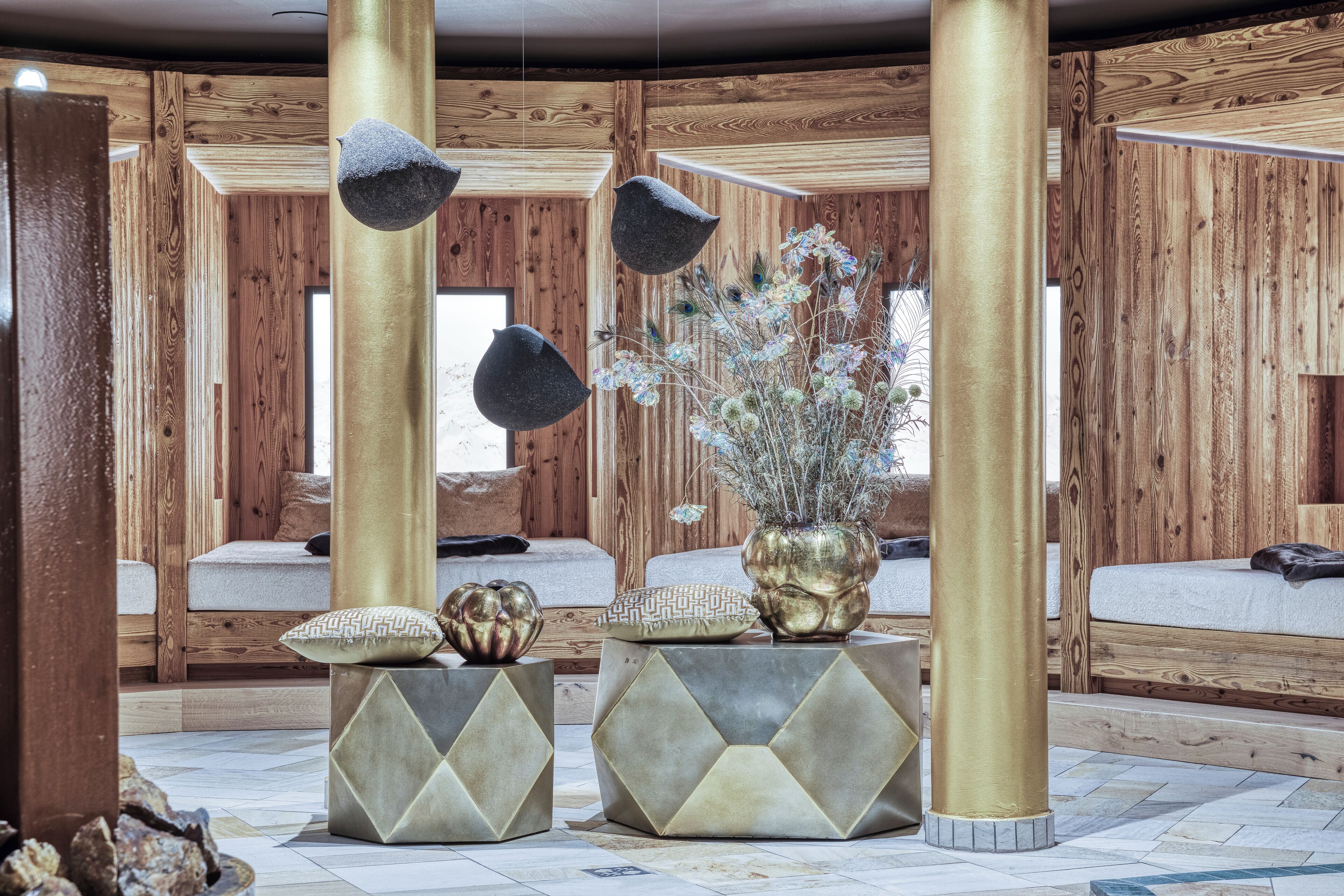 A wooden interior with a bed, a decorative vase, and geometric stools.