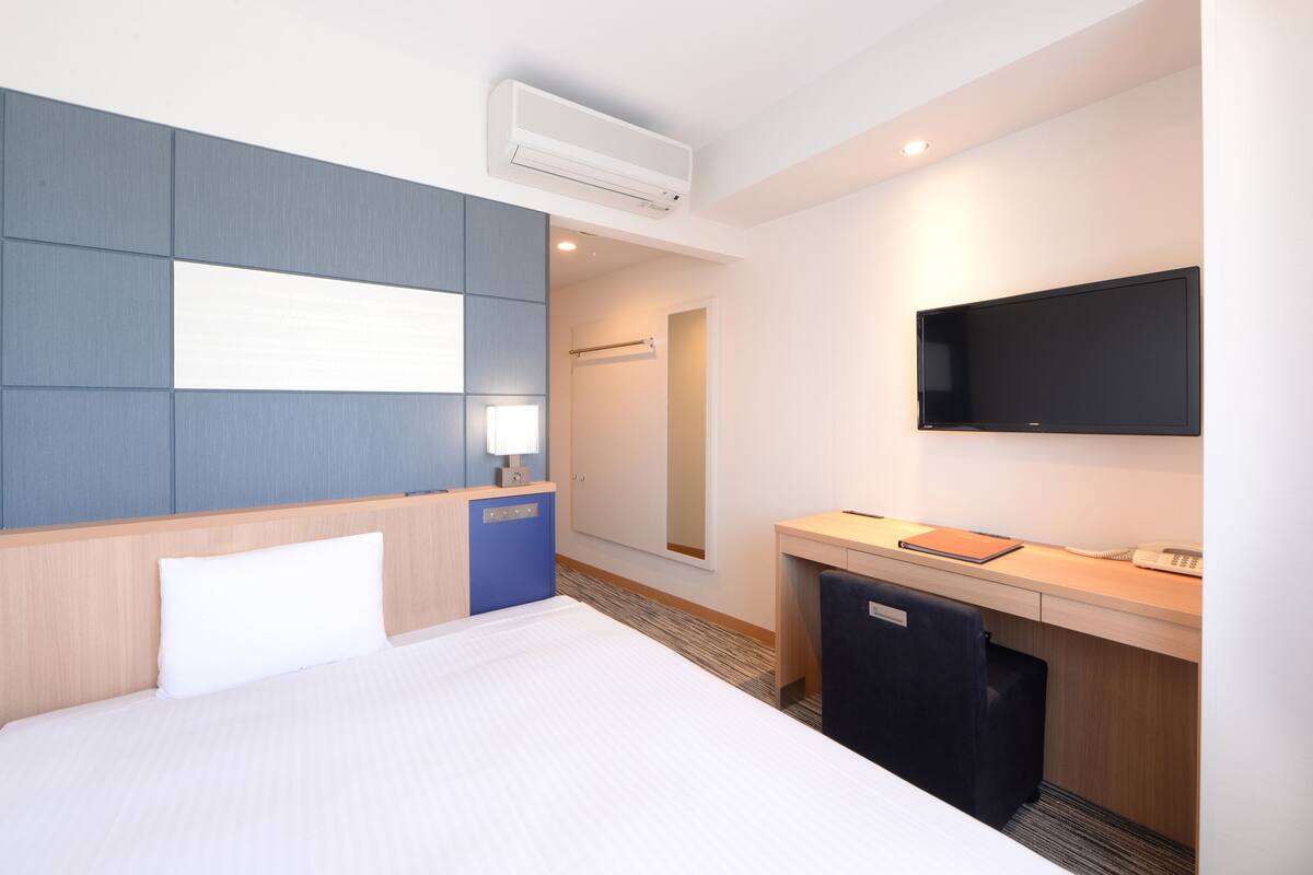 A hotel room with a bed, a desk, a TV, and a wardrobe.