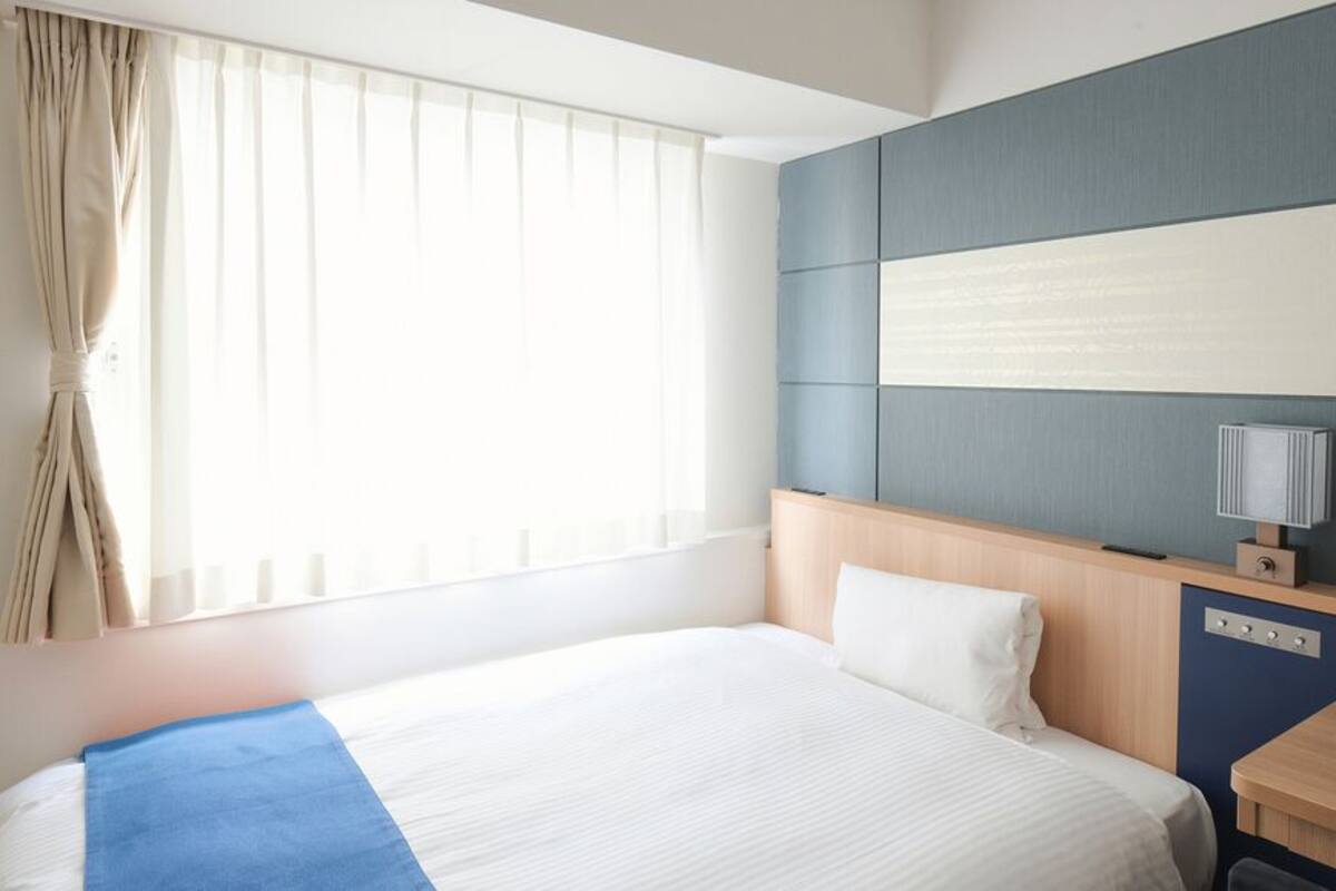 A hotel room with a large bed, a desk, a lamp, and a window with curtains.