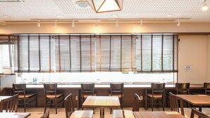 A restaurant with wooden tables and chairs, large windows with blinds, and ceiling lights. - Vessel Inn Ueno Iriya Station (Tokyo)