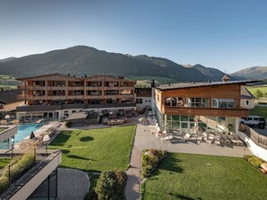 Un hotel de varios pisos con terraza al aire libre y piscina, rodeado de montañas.