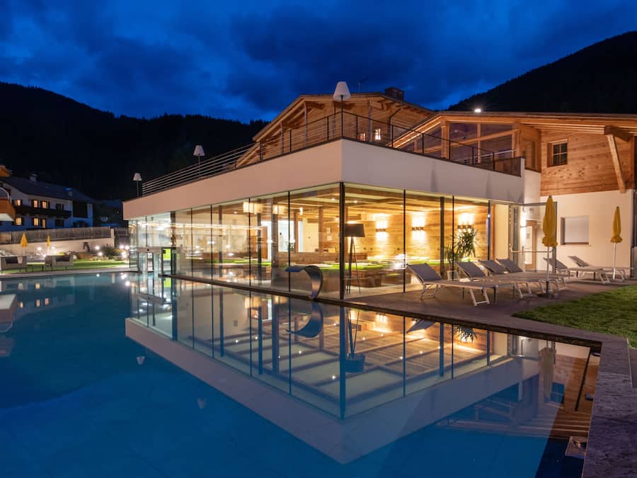Un hotel moderno con piscina de vidrio, mobiliario exterior y fachada de madera.