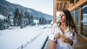 Una persona sosteniendo un vaso de bebida en un balcón con vista a una montaña nevada.