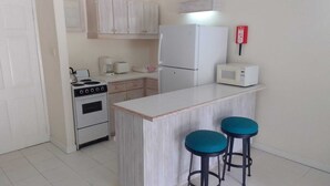 Cocina compacta con estufa, microondas, refrigerador y taburetes de bar.