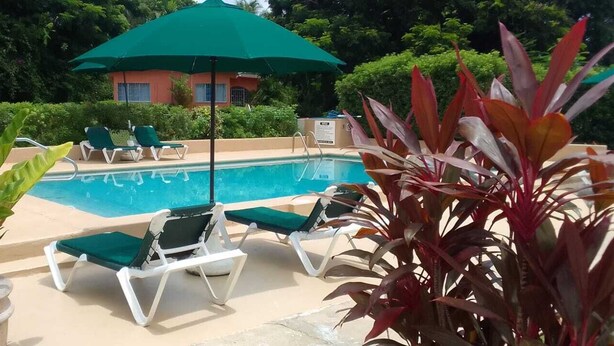 Un área de piscina con sillones de descanso y un paraguas verde.