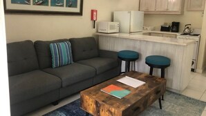 Una sala de estar con un sofá gris, una mesa de centro de madera y dos taburetes azules.