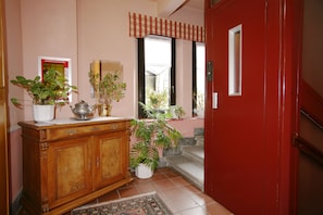 A hallway with a wooden cabinet, potted plants, a red door, and a tiled floor. - Hotel Ruitor (Arvier)