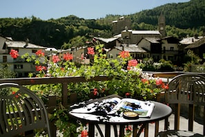 A table with a book and a postcard, surrounded by chairs, with a view of a village and a church in the background. - Hotel Ruitor (Arvier)