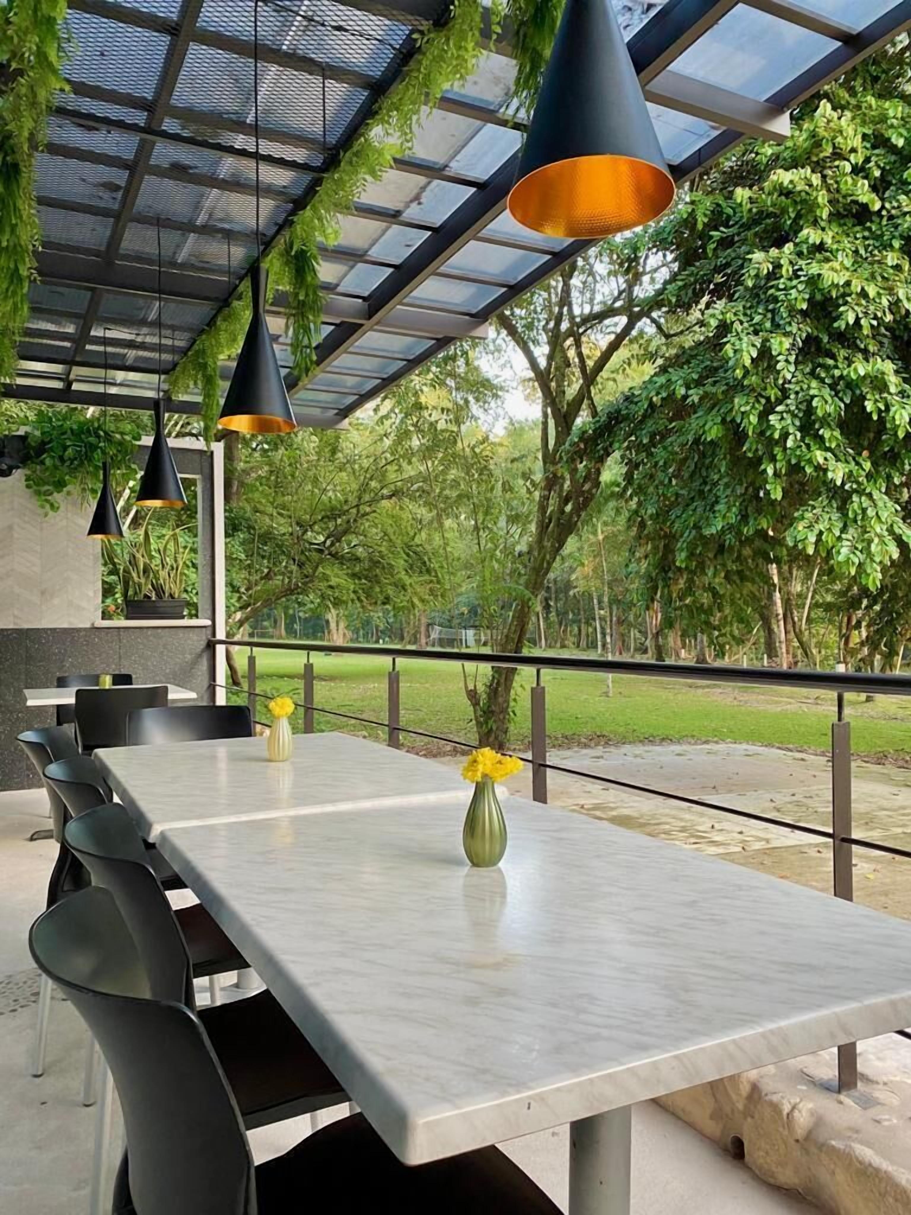 An outdoor dining area with a long table, black chairs, and black pendant lights. There are two yellow flower vases on the table.