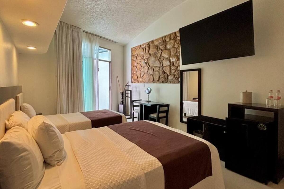 Habitación de hotel con dos camas, un escritorio, un televisor y una pared de piedra.