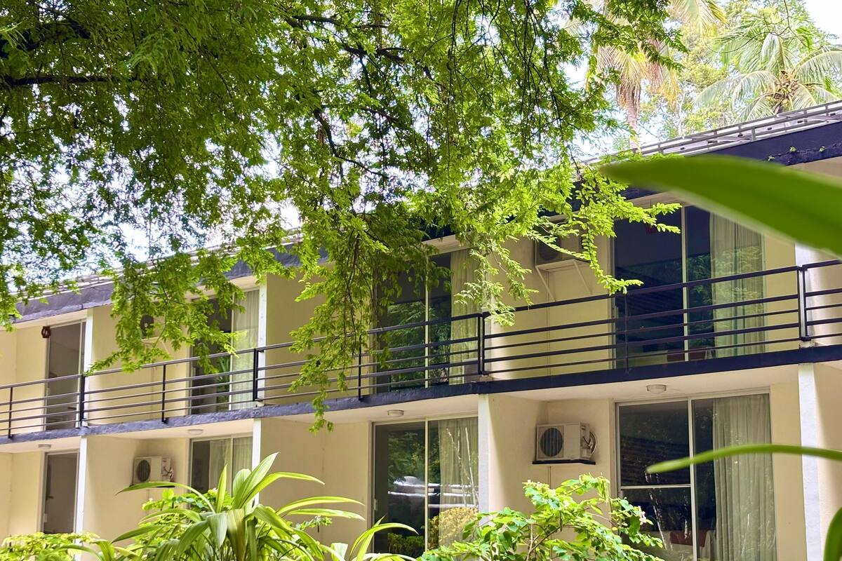 Un edificio de varios pisos con balcones, ventanas amplias y un jardín con diversas plantas.