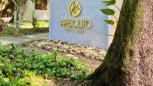 Señalización para 'Arbolito Snack & Bar' con un logotipo, rodeada de follaje y árboles.