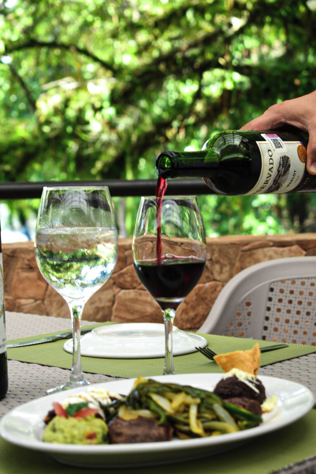 Una botella de vino siendo servida en una copa, con un plato de comida al frente.
