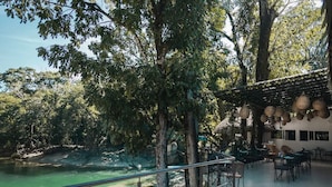 Un restaurante junto al río con terraza al aire libre, con vistas a un río cristalino, rodeado de árboles.