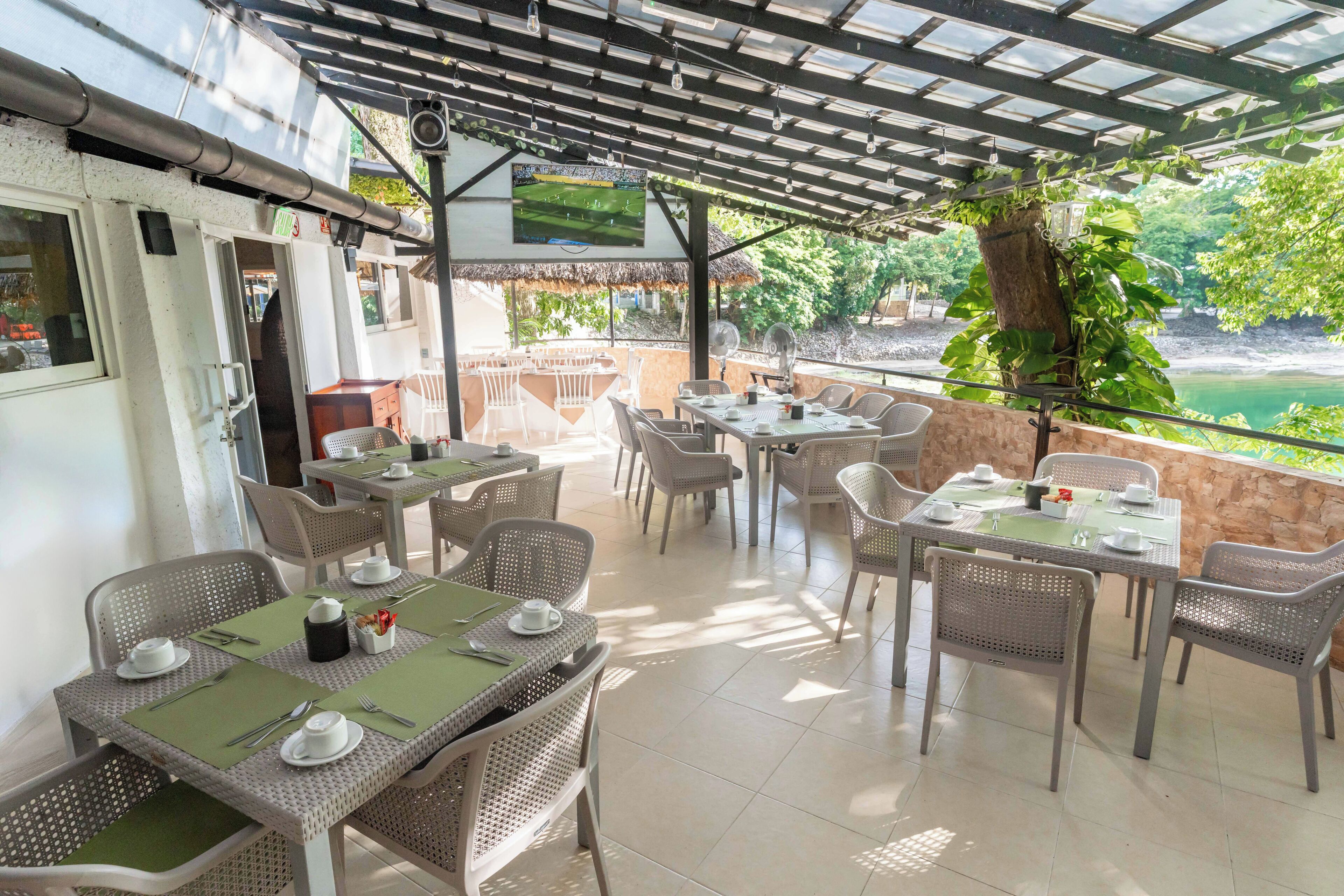 An outdoor patio with tables and chairs, a TV screen, and a view of a body of water.