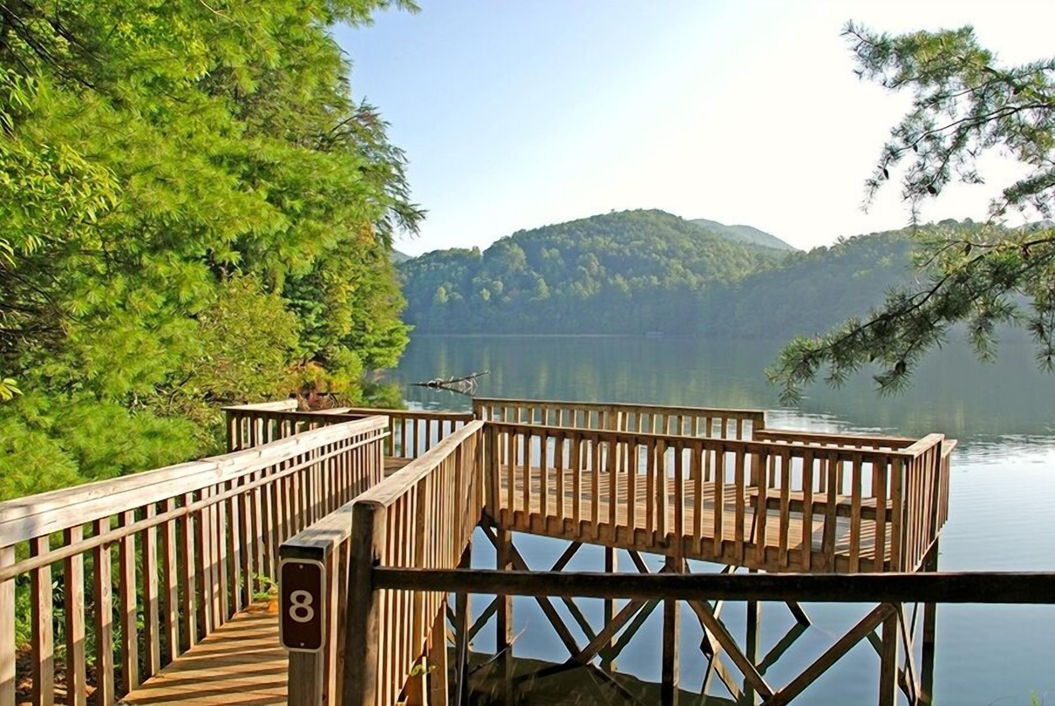 A wooden dock with a railing, a number '8' sign, and a view of a lake with mountains in the background.
