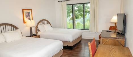 A hotel room with two beds, a wooden table, a TV, and a window with curtains.