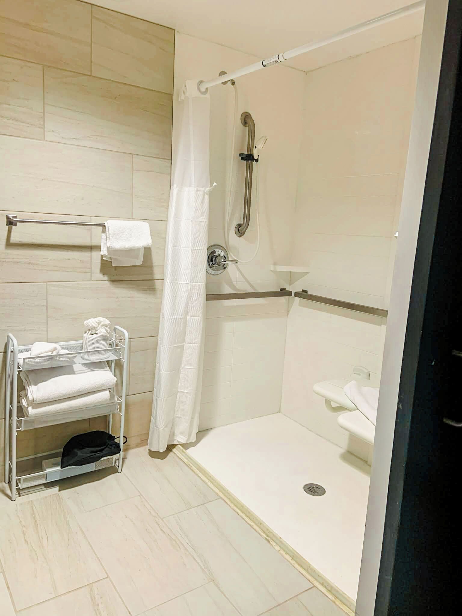 A modern bathroom with a walk-in shower, a towel rack, and a shelf with towels.