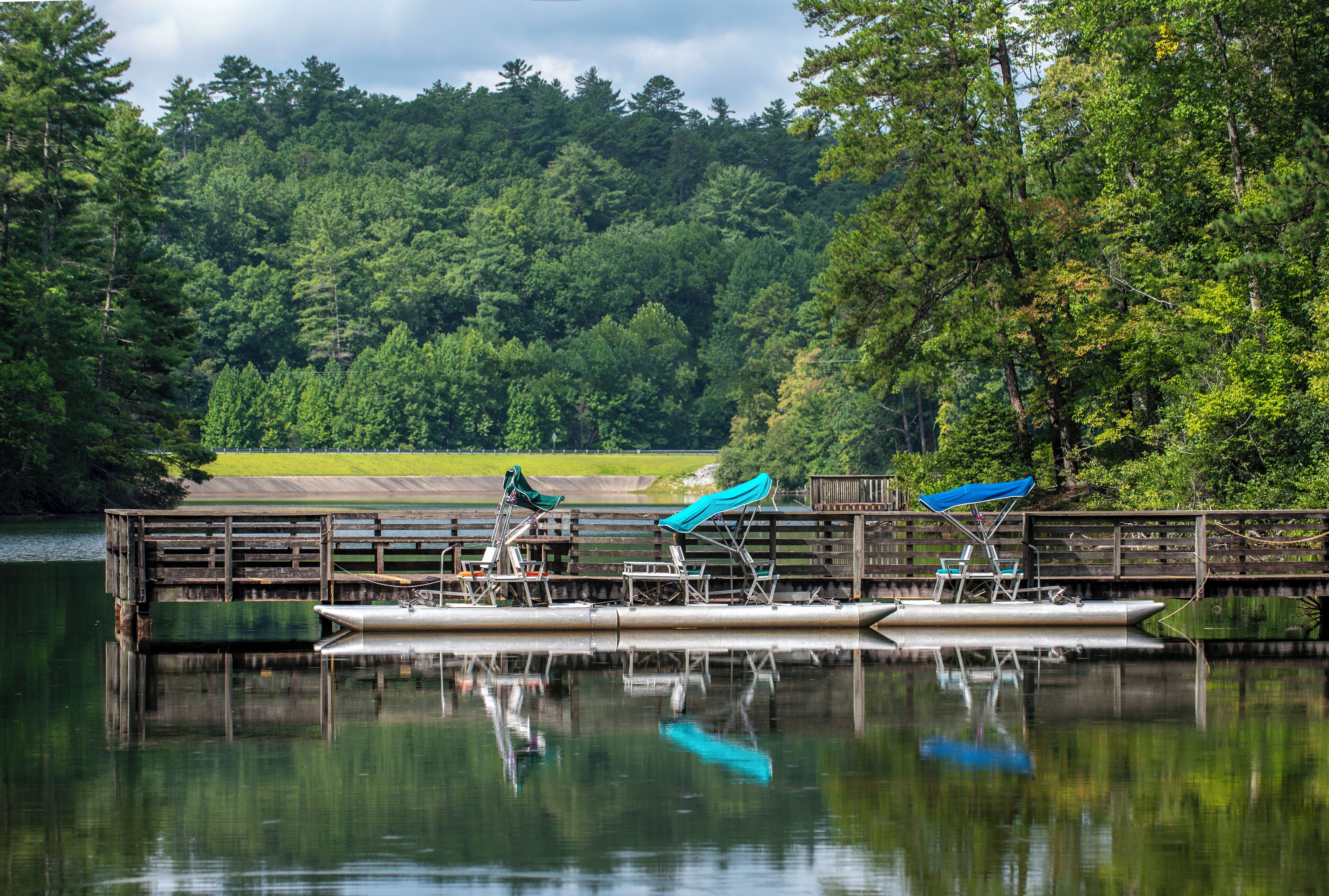 A calm lake with a dock, chairs, and a boat.