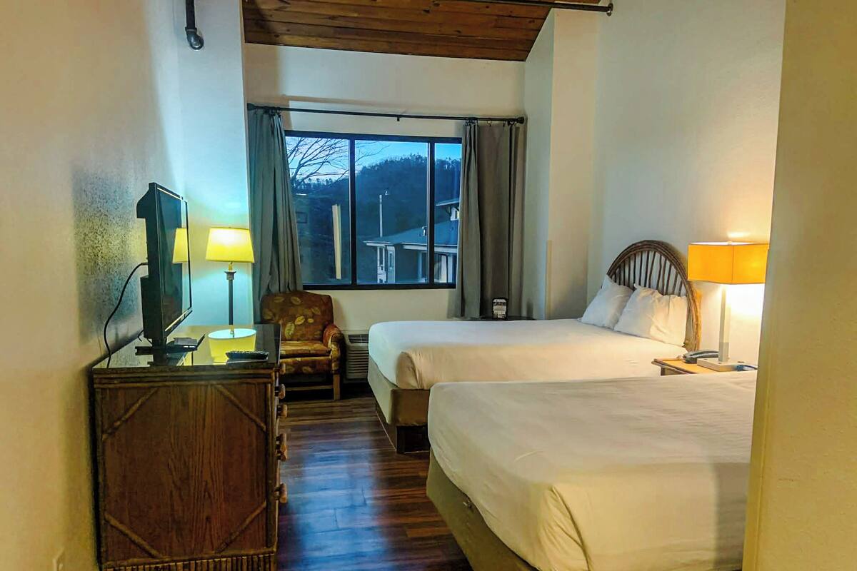 A hotel room with two beds, a desk with a television, a chair, and a window with curtains.
