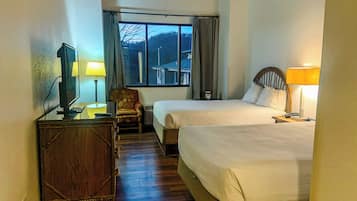 Ett hotellrum med två sängar, ett skrivbord med en tv, en stol och ett fönster med gardiner.