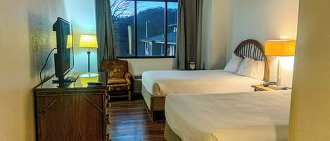 A hotel room with two beds, a desk with a television, a chair, and a window with curtains.