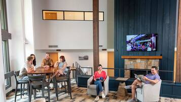 A spacious indoor area with a wooden ceiling and a stone fireplace. There are multiple seating areas with chairs and sofas, and a television mounted on the wall.