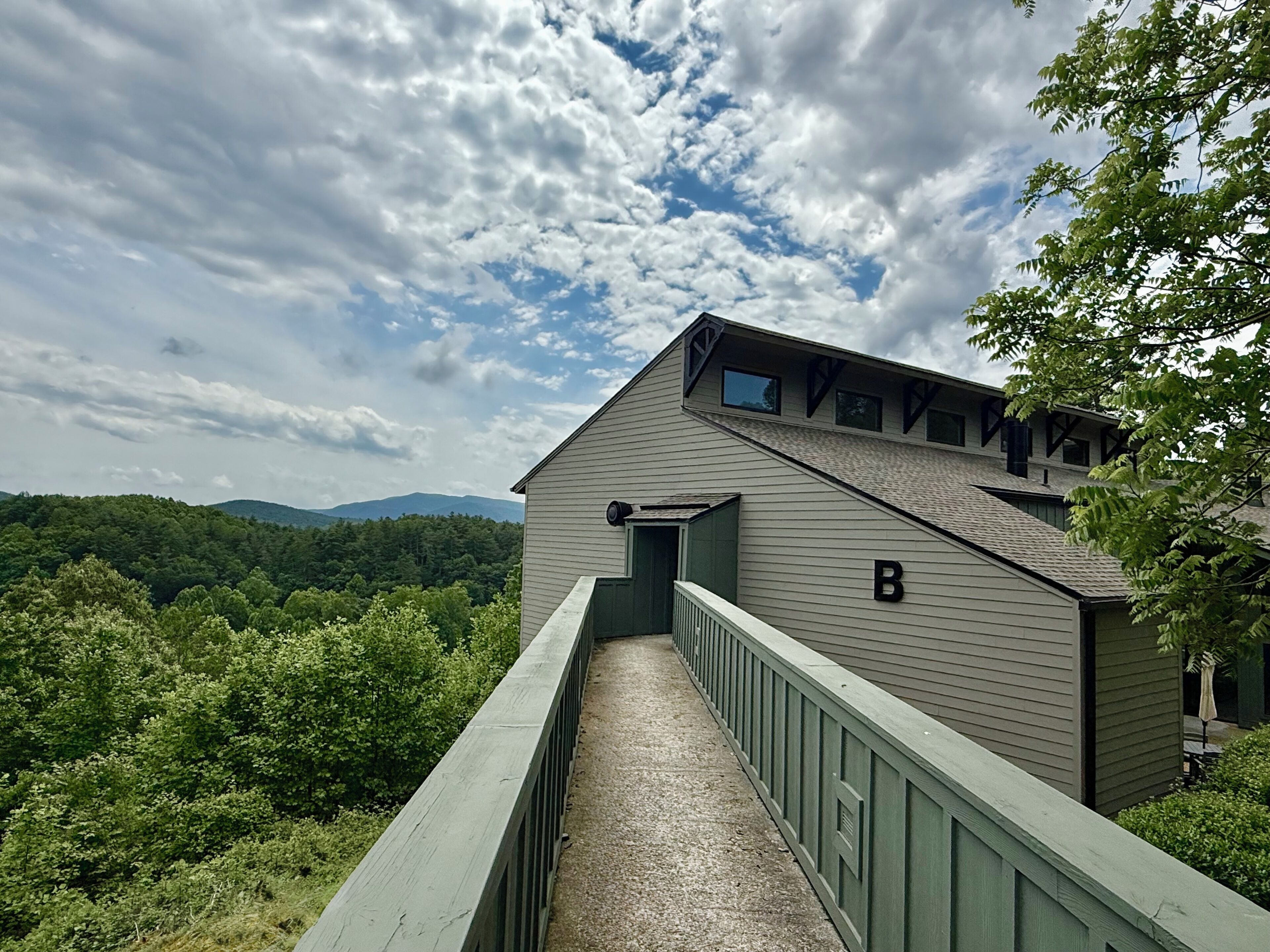 A building with a green exterior, a covered walkway, and a view of a forested area with mountains in the distance.