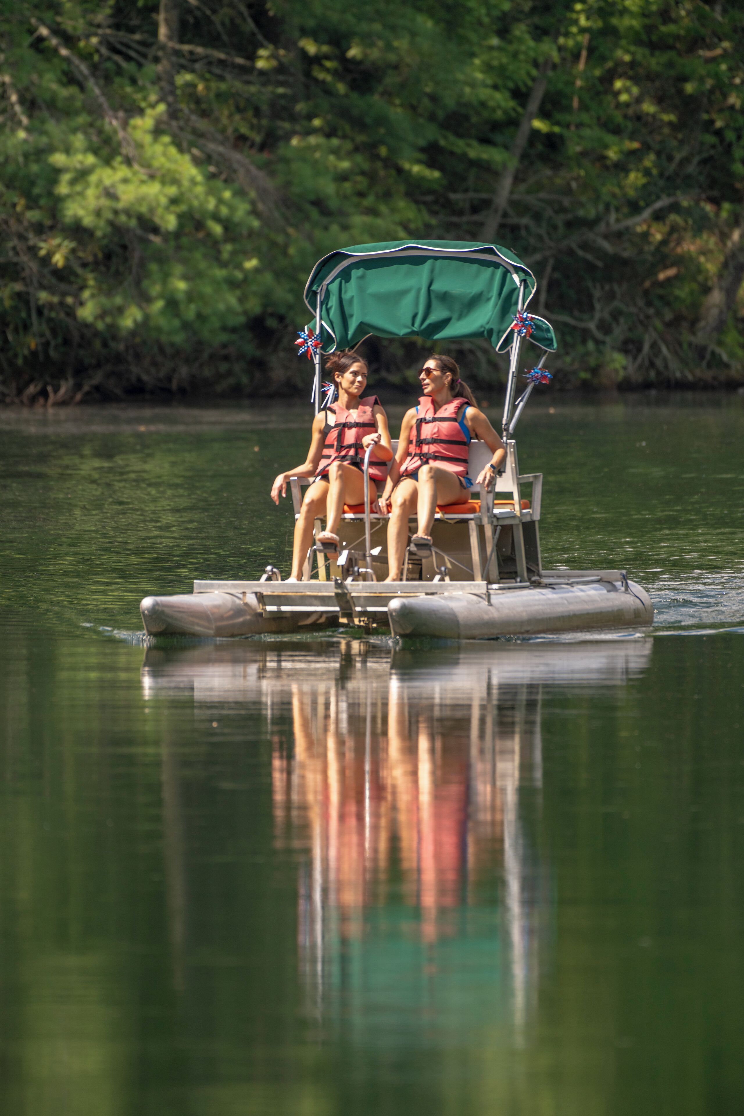 Two people on a small, motorized boat with a canopy, floating on calm water surrounded by greenery.