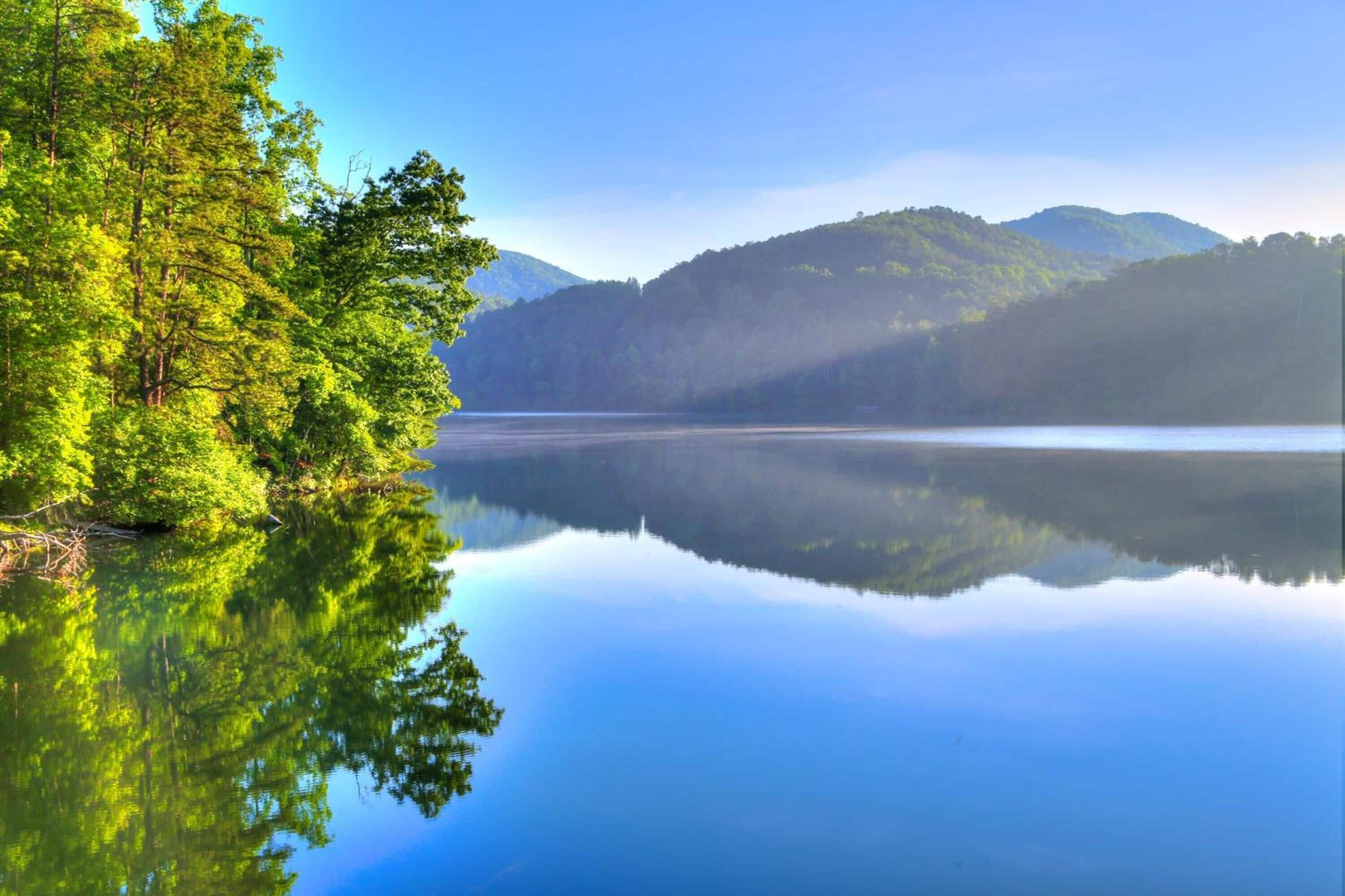 A calm lake with reflections of trees and mountains.