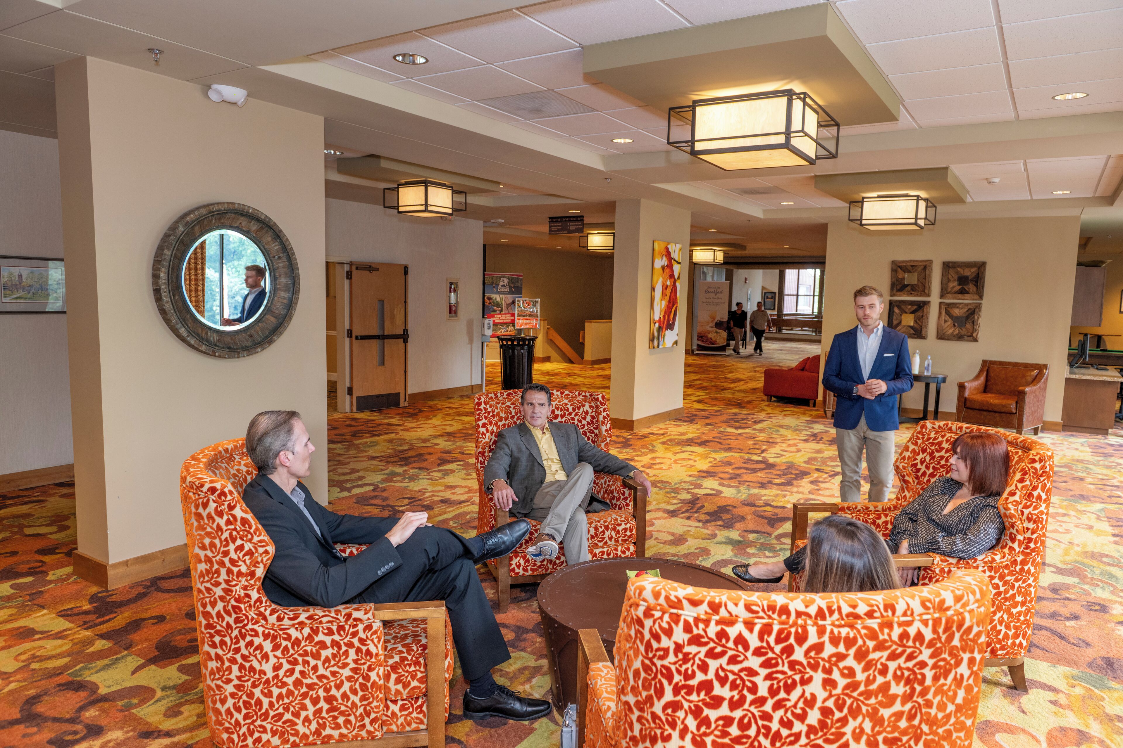 A hotel lobby with patterned orange and white chairs, a round mirror, and a large wooden table.