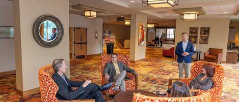 A hotel lobby with patterned orange and white chairs, a round mirror, and a large wooden table.