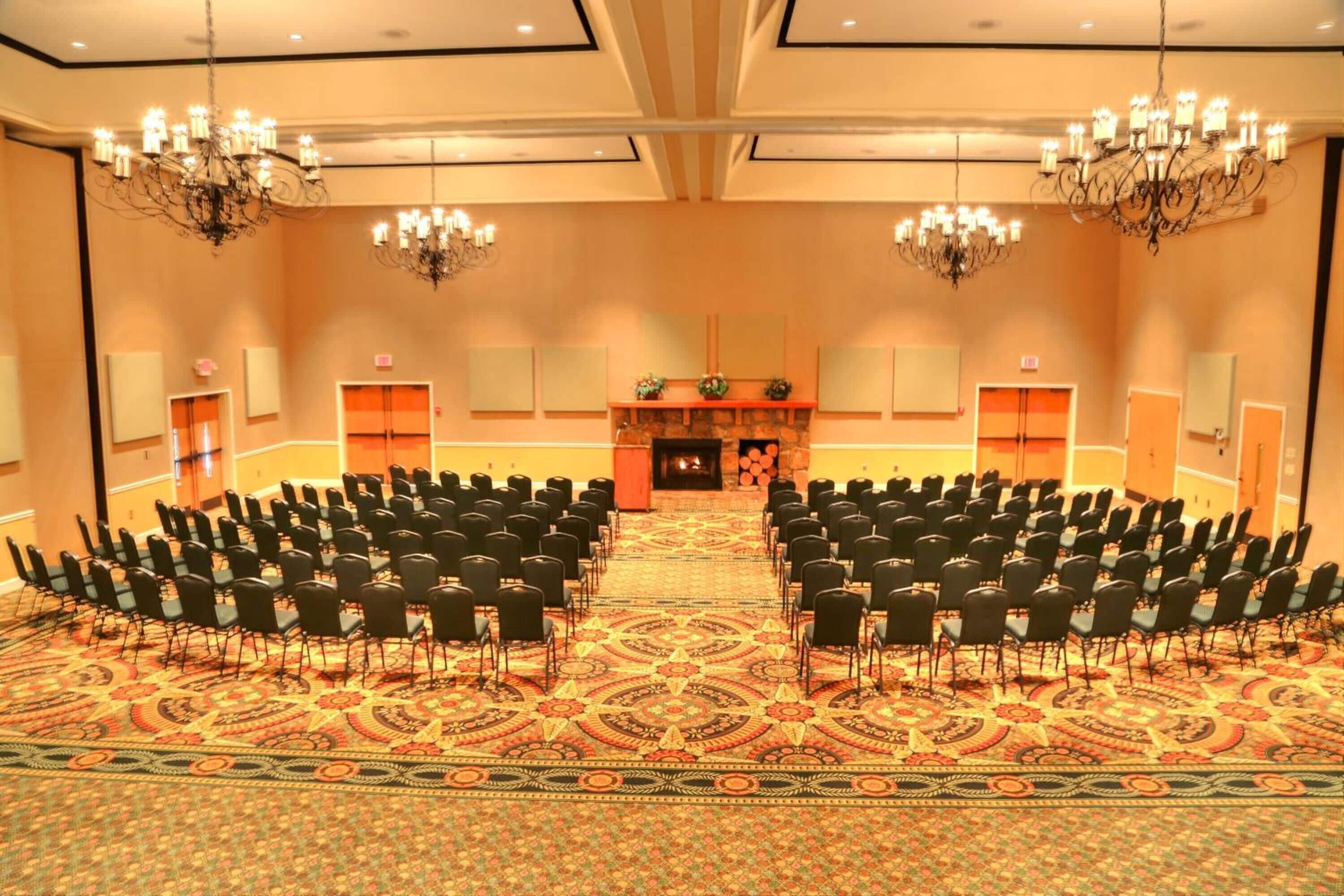 A large conference room with rows of chairs facing a stage with a fireplace.