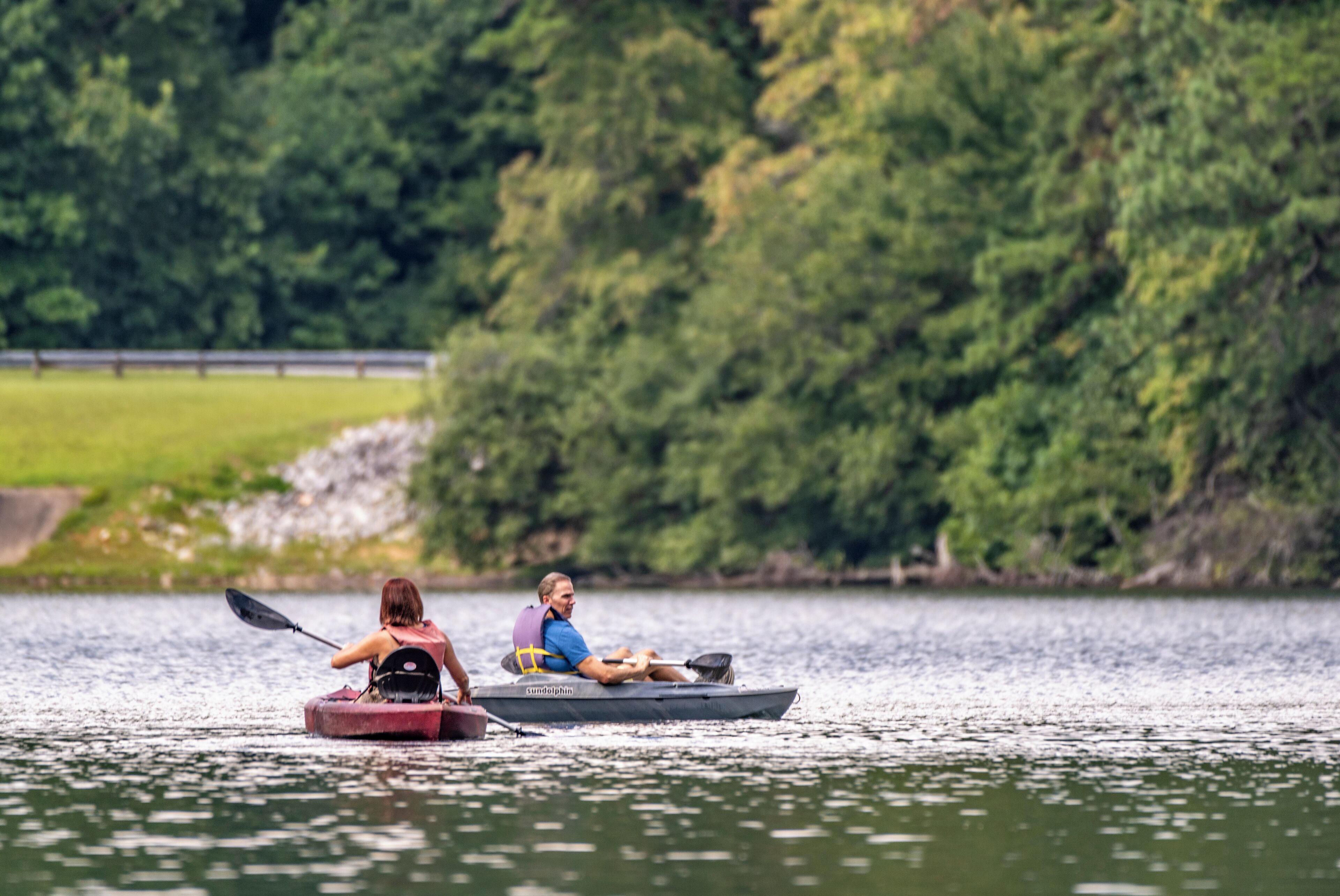 Two people kayaking on a calm lake surrounded by dense greenery.