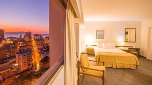 Una habitación de hotel con cama, mesita de noche, silla y vista a la ciudad.