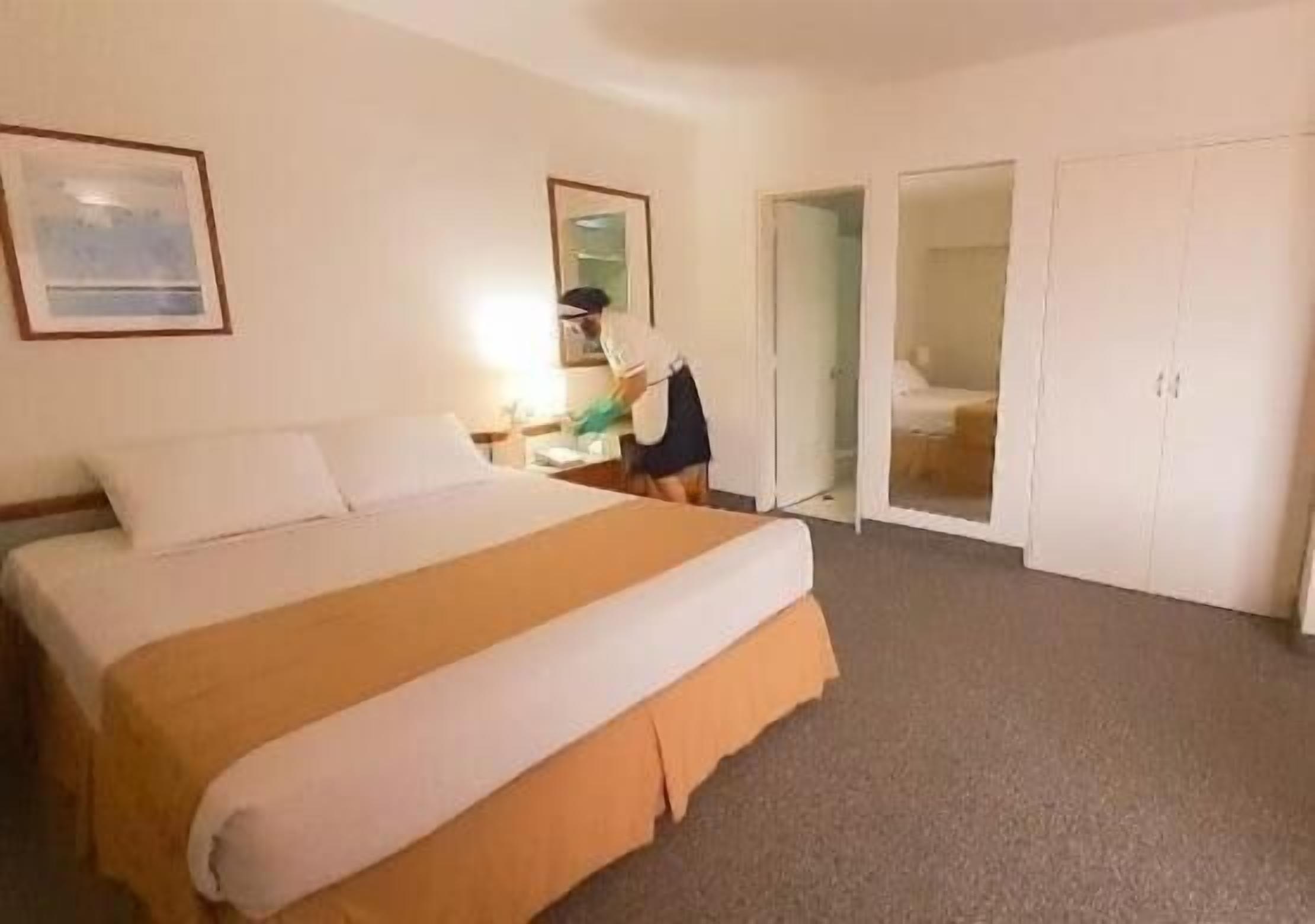 A hotel room with a large bed, a desk, a chair, and a wardrobe.