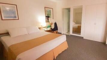 A hotel room with a large bed, a desk, a chair, and a wardrobe.