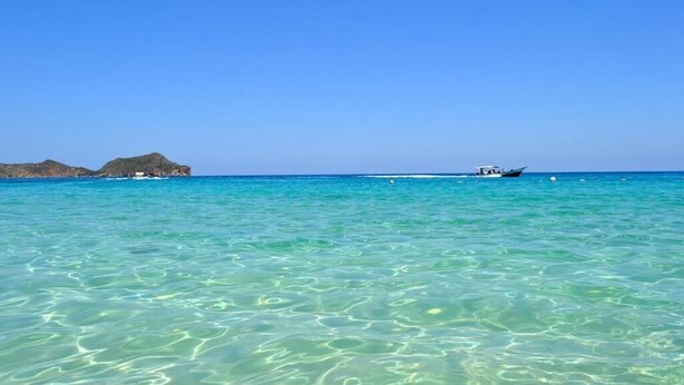 Mar azul y transparente con barcos y una isla distante.
